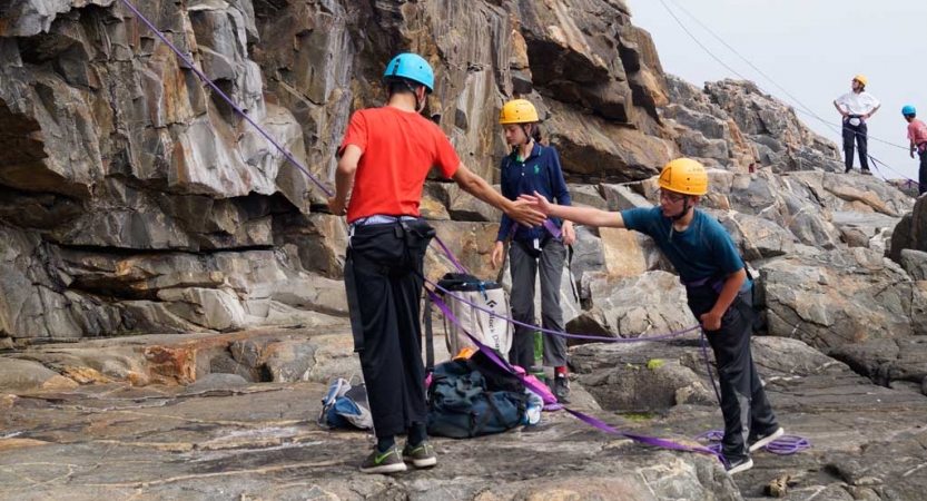 Two people wearing safety gear high five a the bottom of a rock wall. 